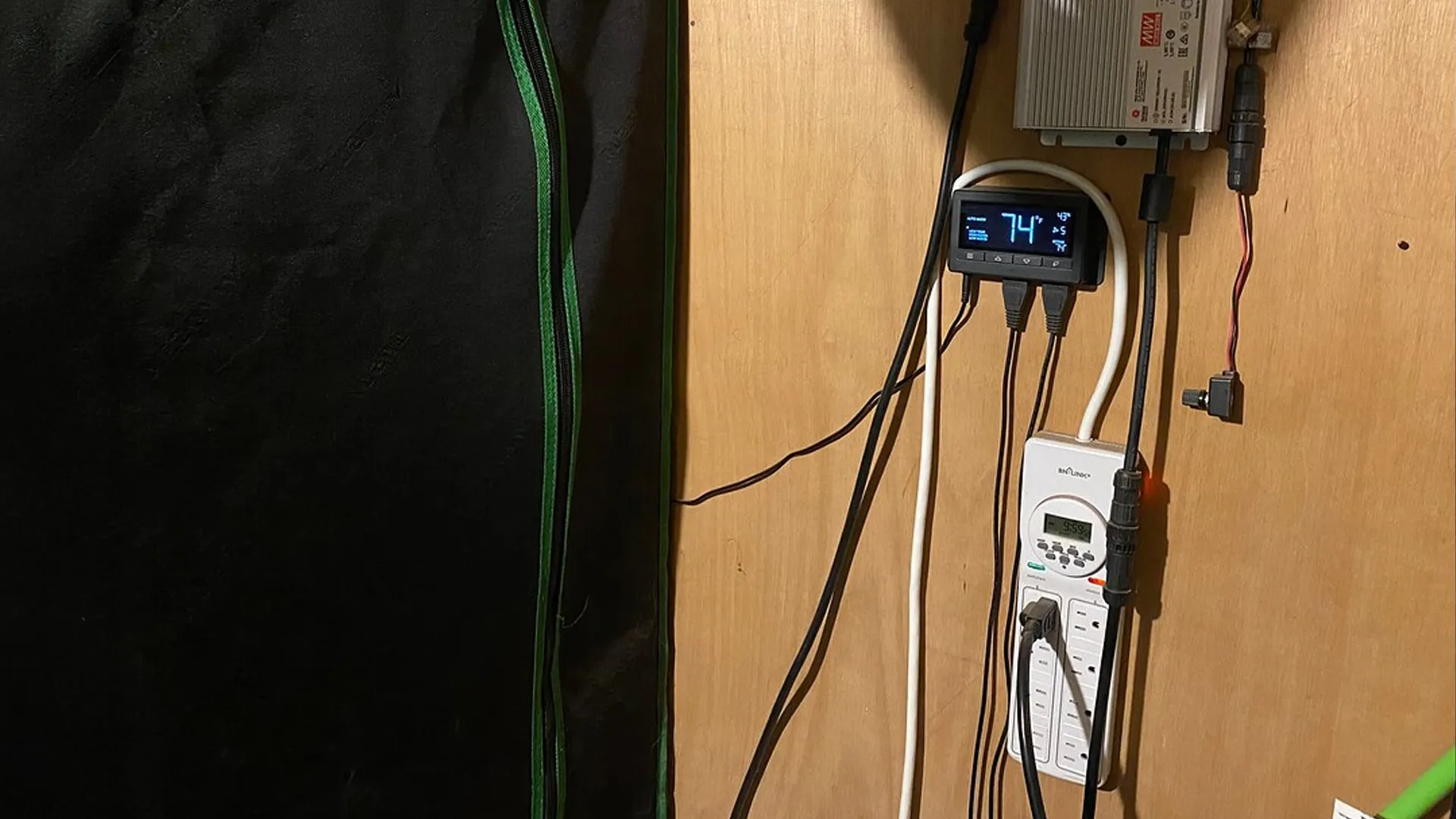 A wooden wall with electronic devices, cables, and a digital temperature display showing 74°F. A black curtain is partially visible on the left.