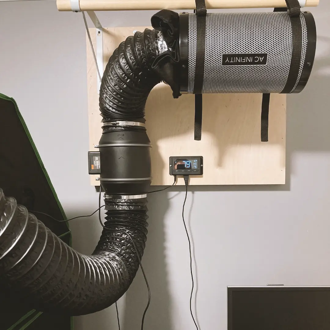 Ventilation system with a black flexible duct attached to a wall-mounted air filter. Two digital displays show environmental data.